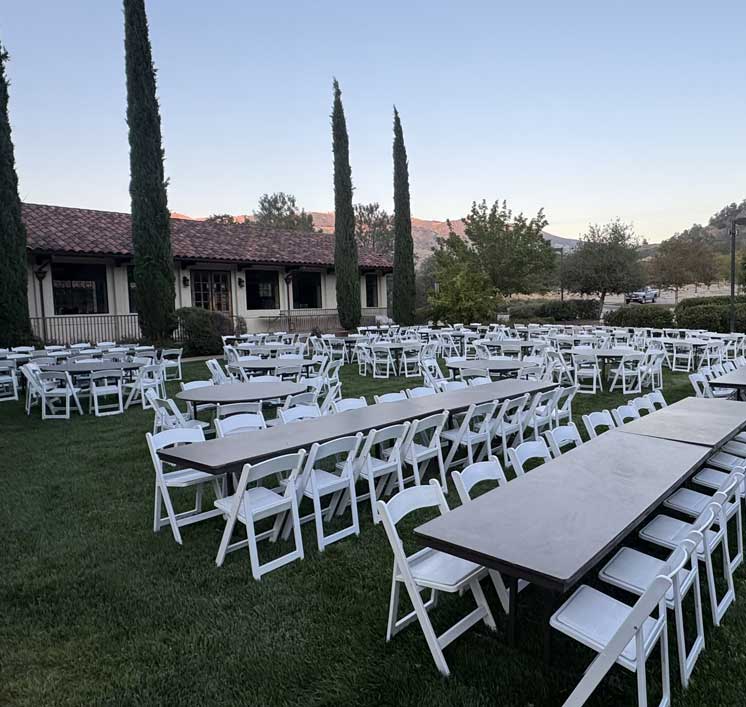 White folding chairs and banquet tables arranged on the lawn outside Villa La Paz at dusk