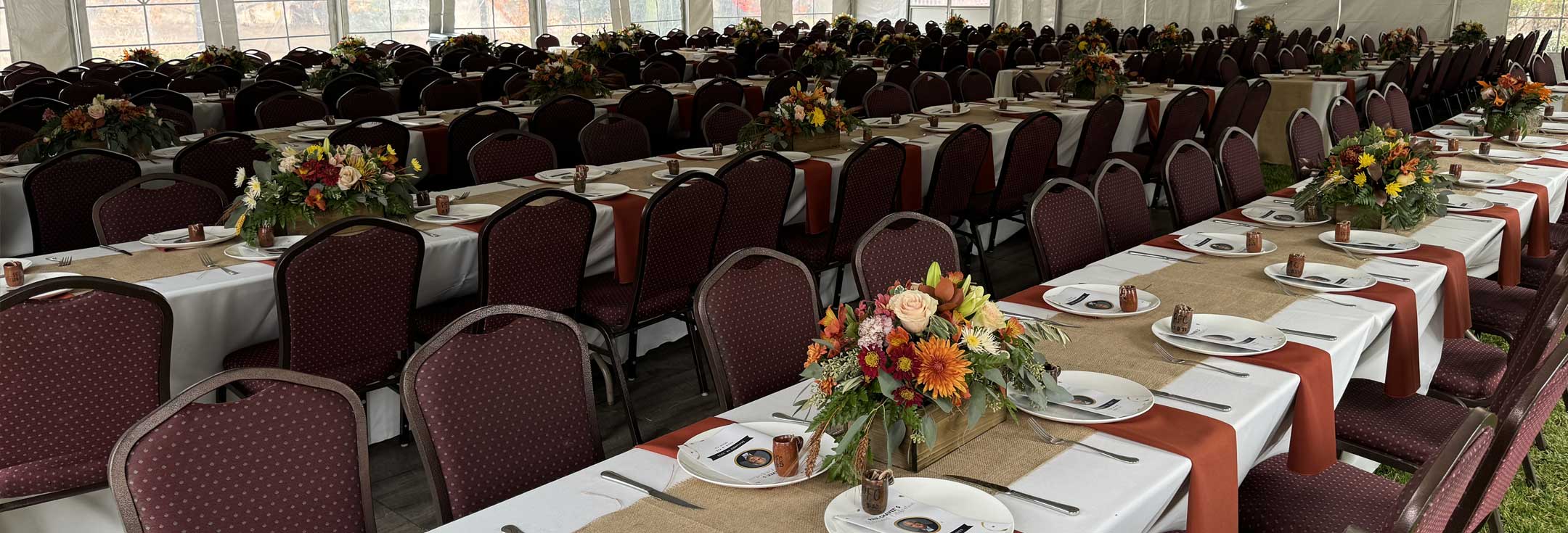 Rows of long banquet tables with burlap runners and autumn flower centerpieces set for a large event