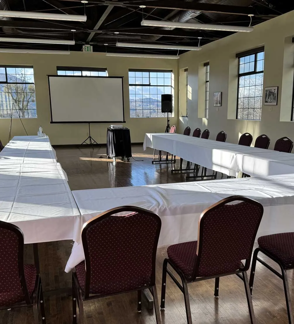Meeting room with U-shaped white-clothed tables, burgundy chairs, and a projection screen