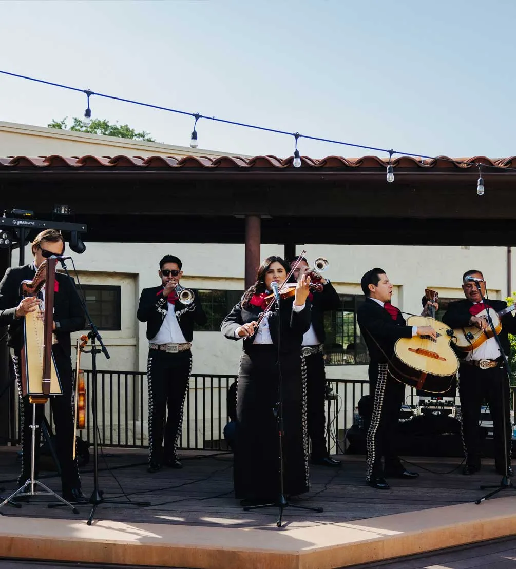 Mariachi band performing on a covered patio stage beneath string lights