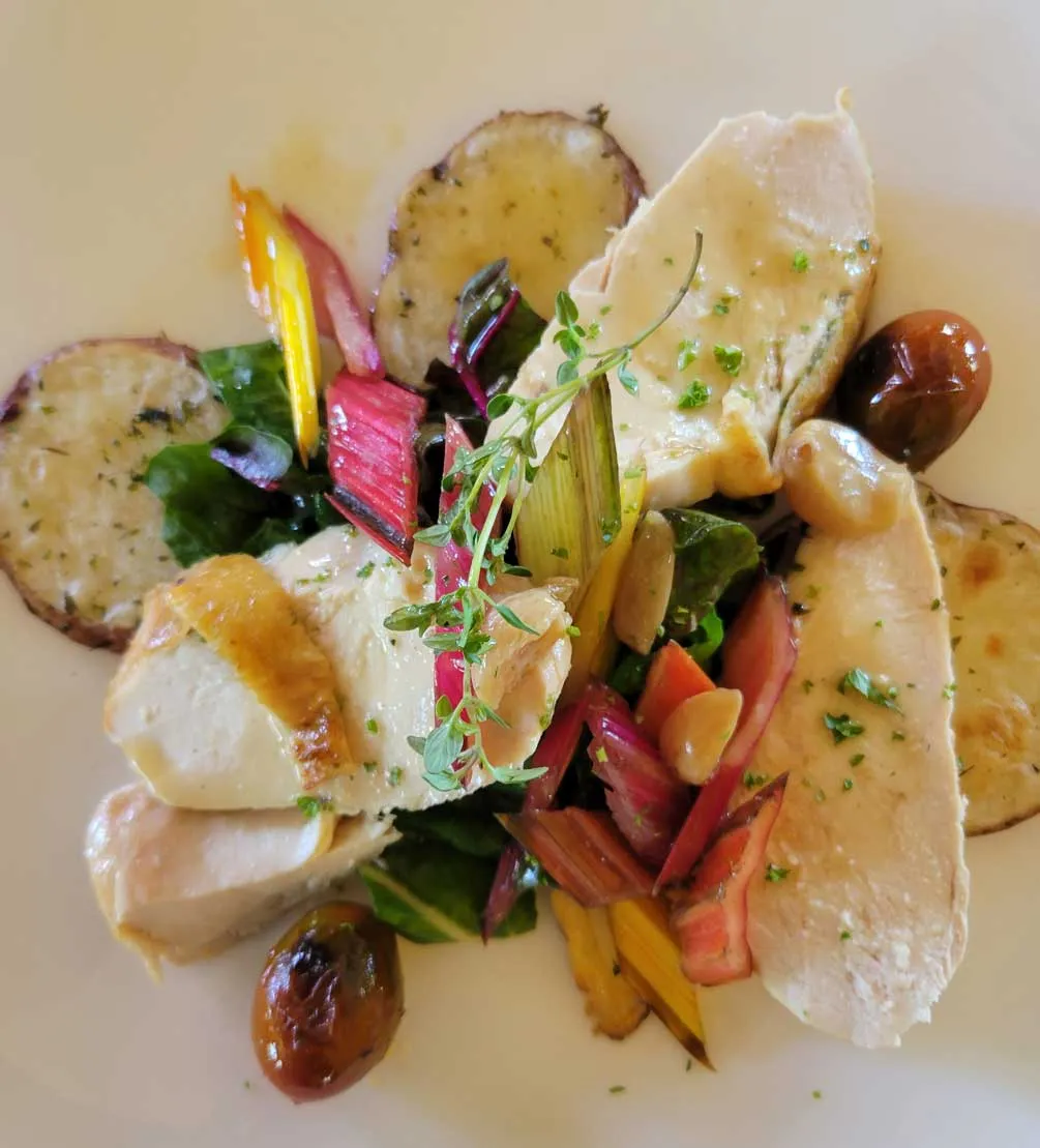 Chef-plated sliced chicken with rainbow chard, roasted potatoes, and blistered grapes