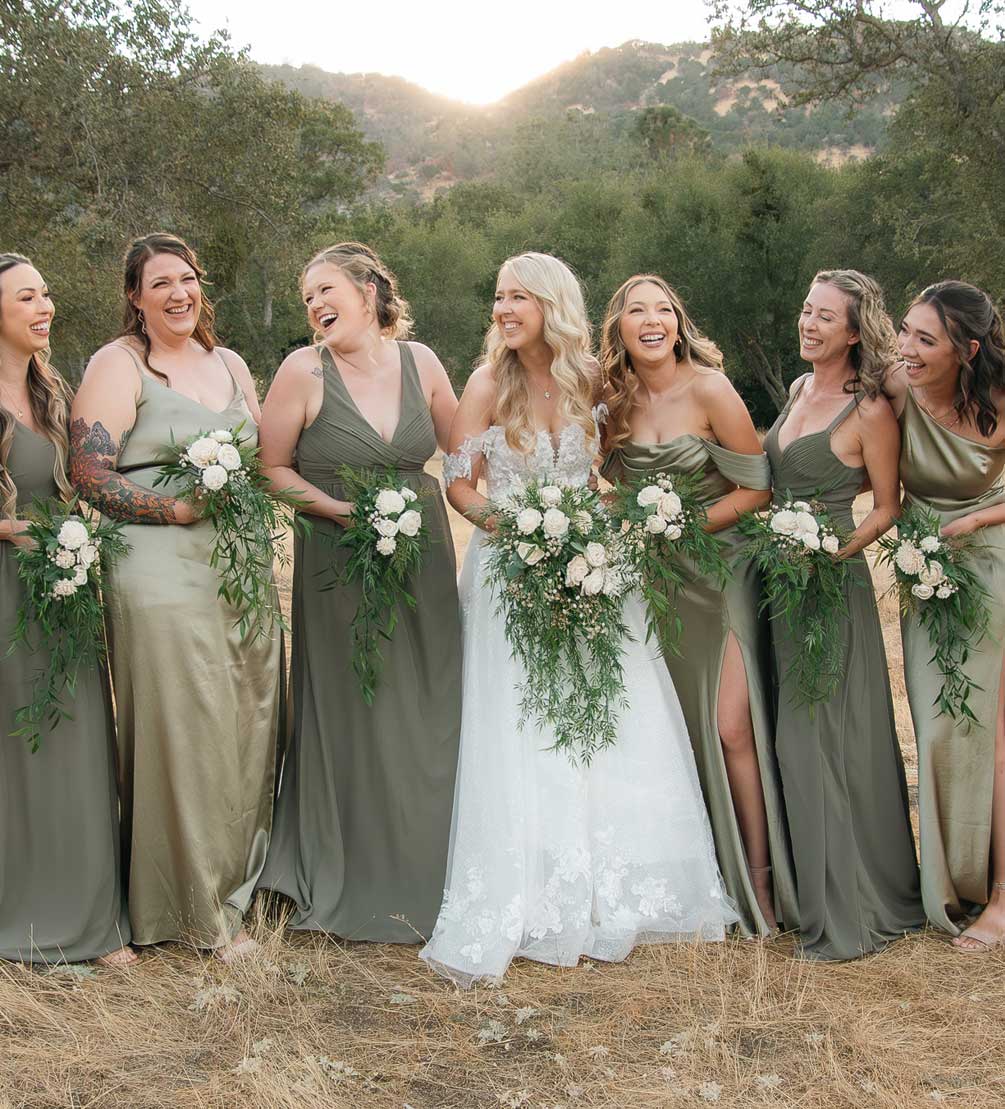 Bride laughing with six bridesmaids in sage green dresses against golden foothills