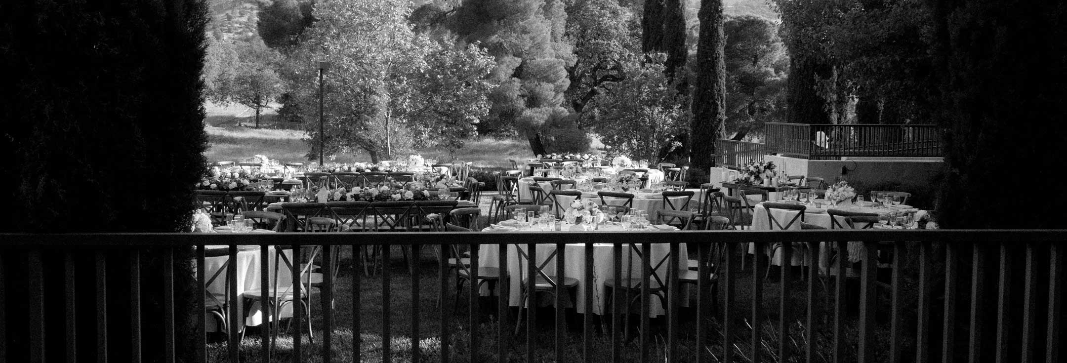 Black-and-white view of round reception tables set beneath trees on the Villa La Paz grounds