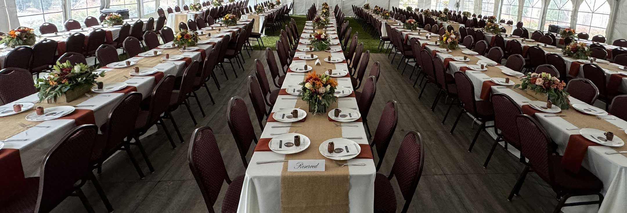 Long banquet tables set with place settings and autumn floral centerpieces inside an event tent