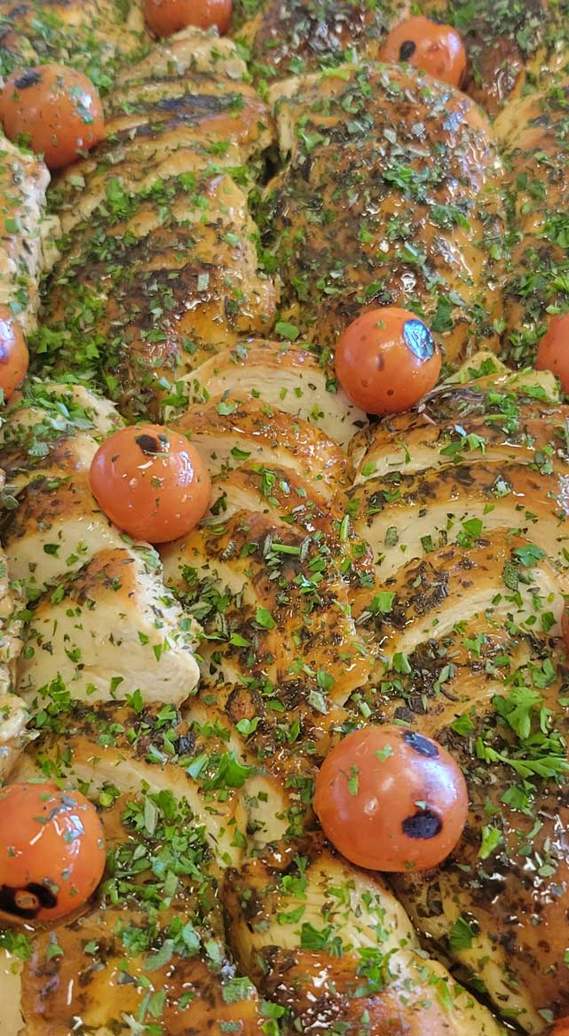 Herb-crusted sliced chicken breasts topped with blistered cherry tomatoes