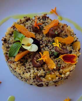 Plated quinoa dish topped with roasted carrots, edible flowers, and microgreens