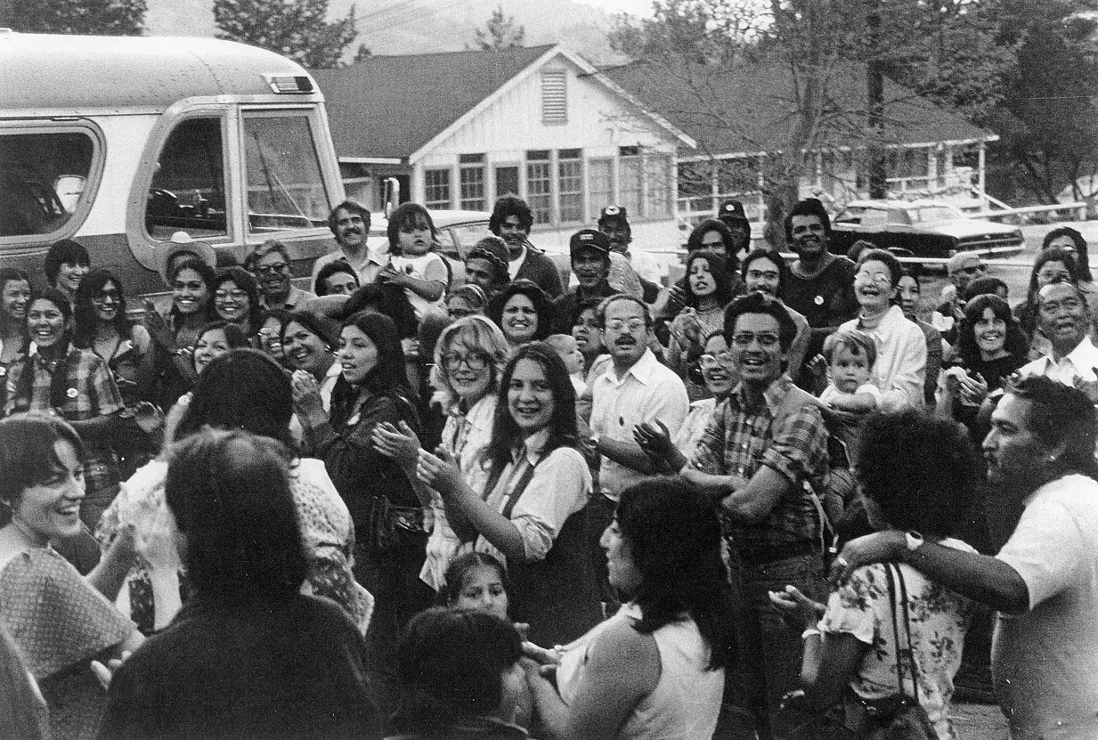 Farm worker families and supporters smiling and applauding beside a bus at La Paz, 1970s black-and-white photo