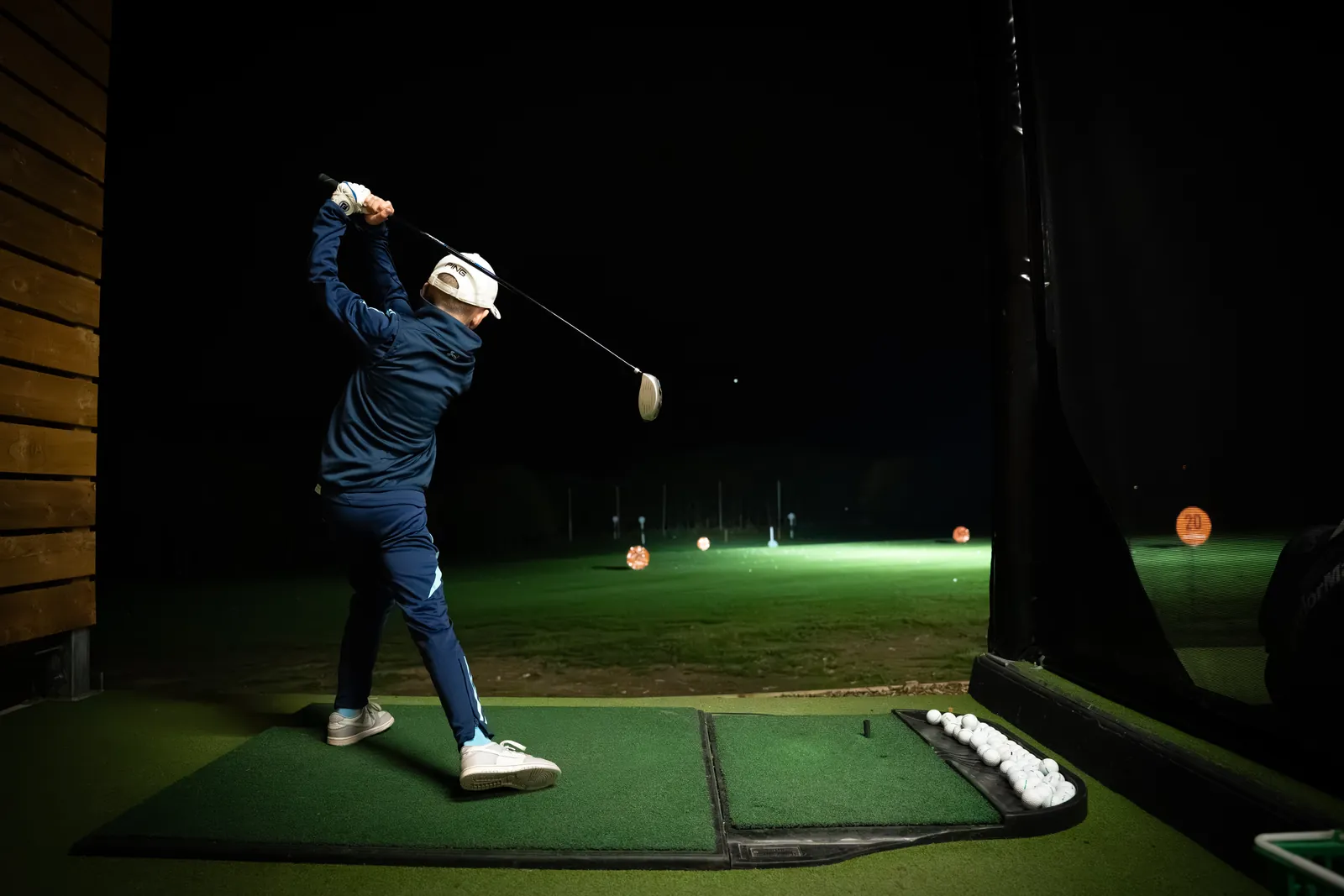 Golfer mid-swing inside an indoor TrackMan bay at Evolution Golf Academy, Derbyshire.