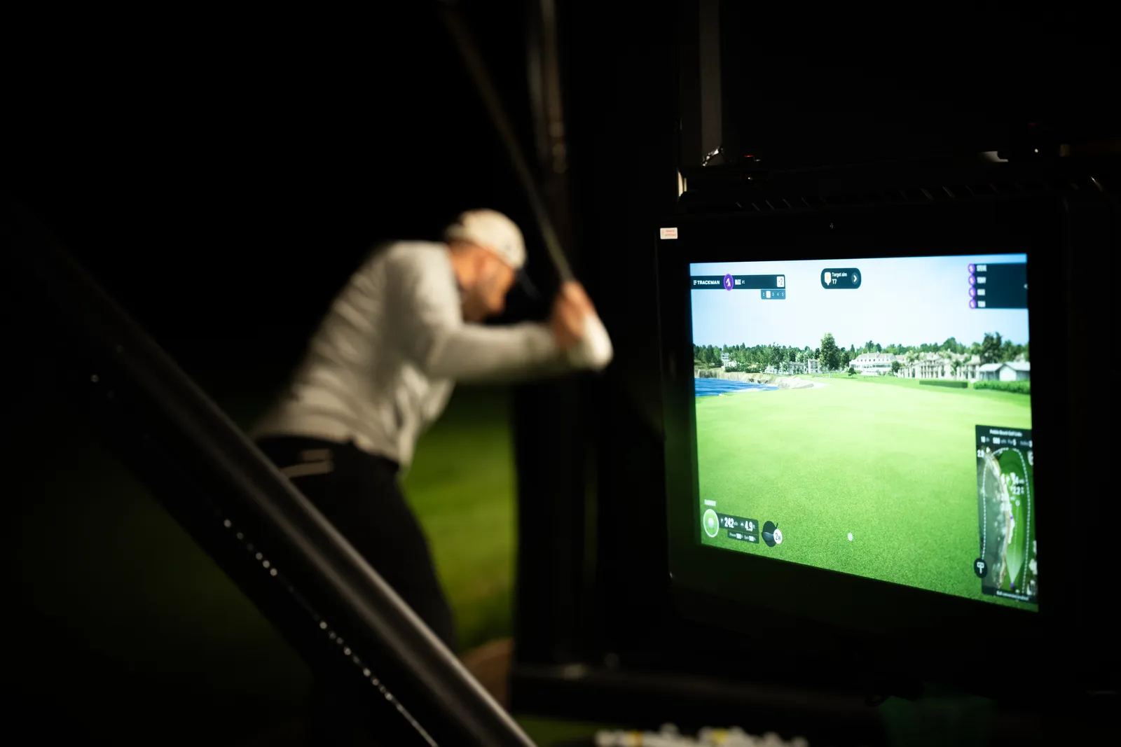 Golfer swinging at the TrackMan screen during an evening session at Evolution Golf Academy.