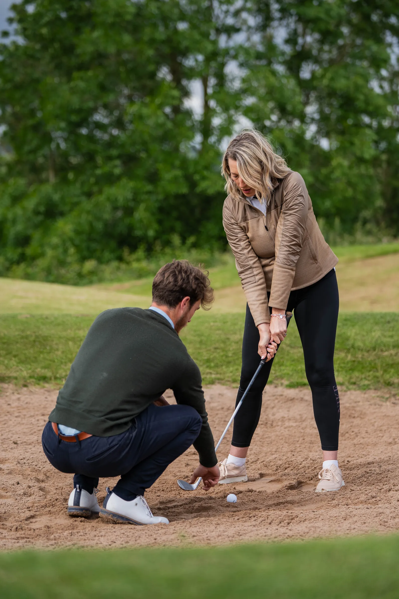 PGA coach kneeling beside a student to demonstrate grip during an on-course golf lesson in Derbyshire.