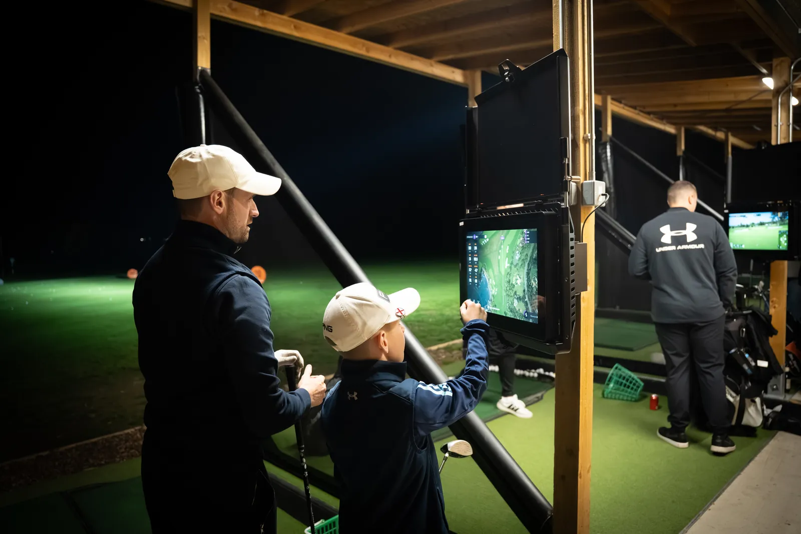 Lit driving range bays at Evolution Golf Academy after dark in Derbyshire.