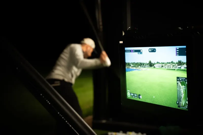 Golfer swinging at the TrackMan screen during an evening session at Evolution Golf Academy.