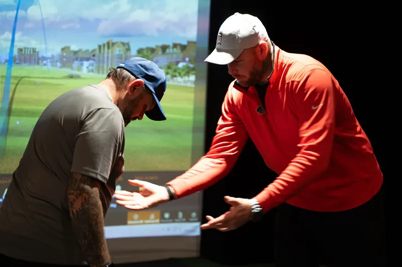 TPI golf movement coaching: coach demonstrating a movement to a student in the TrackMan bay at Evolution Golf Academy, Derby.