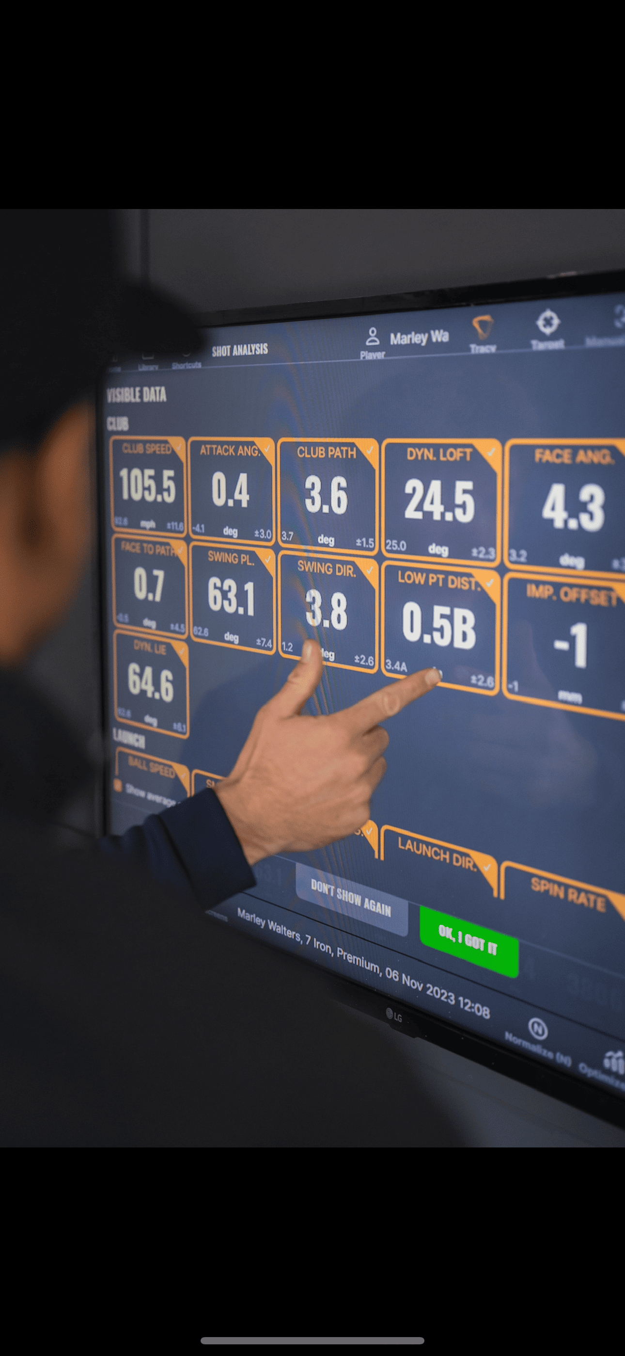 TrackMan screen showing 7 iron swing data while a coach points at the numbers