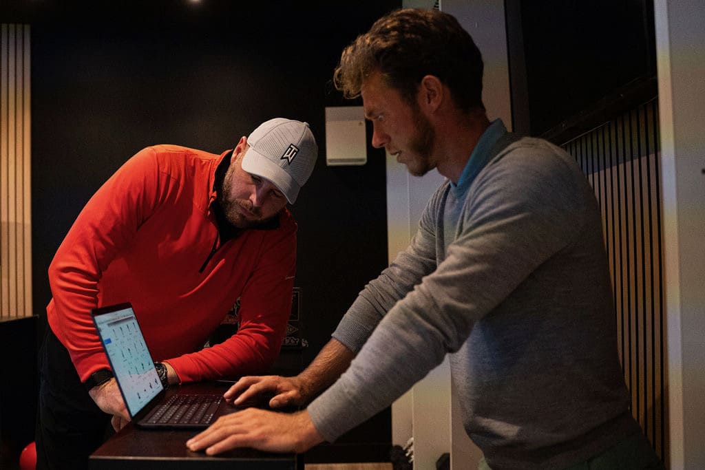 Strength coach guiding a golfer through a squat in the TrackMan bay