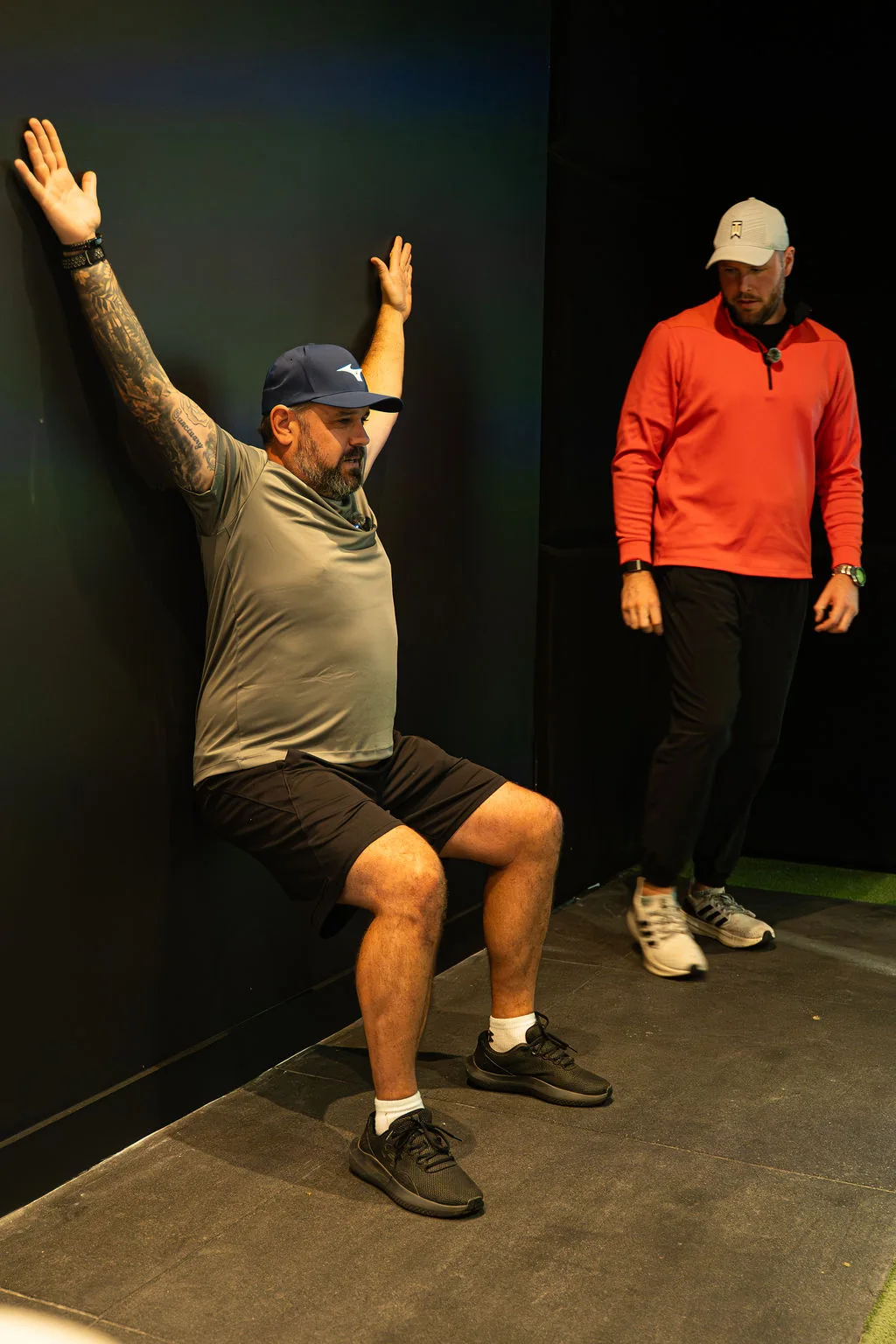 Golfer holding a wall squat with arms overhead during a golf fitness screening while the coach observes at Evolution Golf Academy near Derby