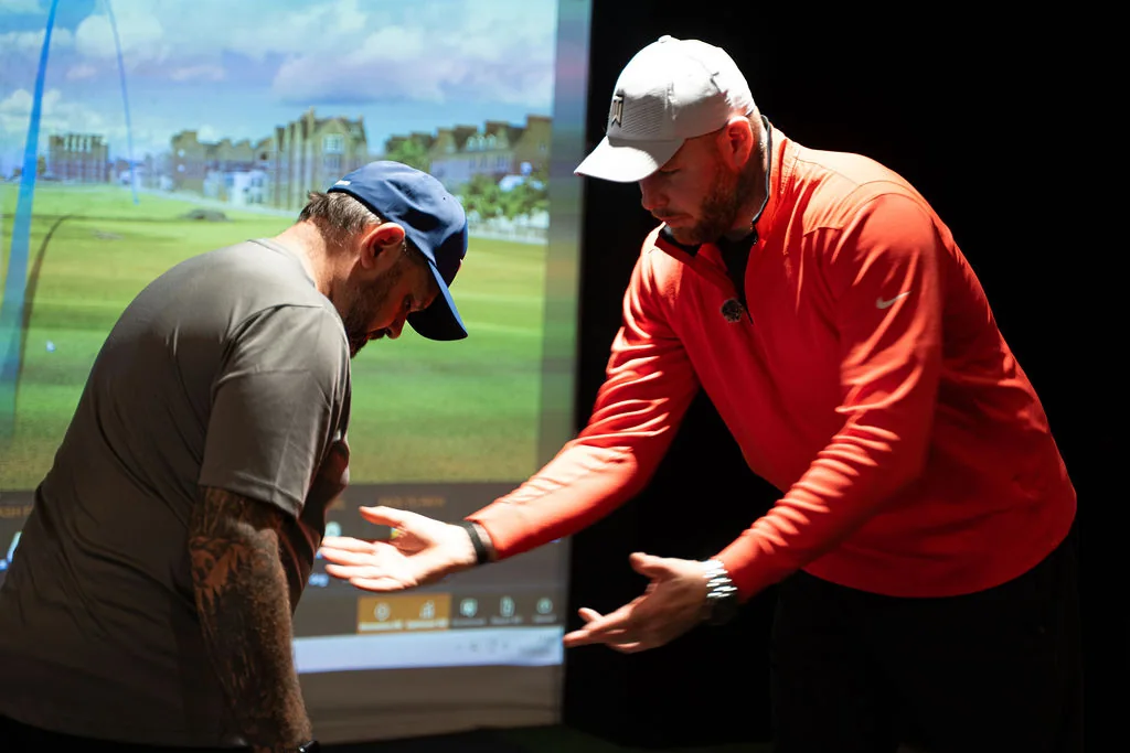 Coach guiding a golfer into the correct posture in front of the TrackMan screen at Evolution Golf Academy near Derby