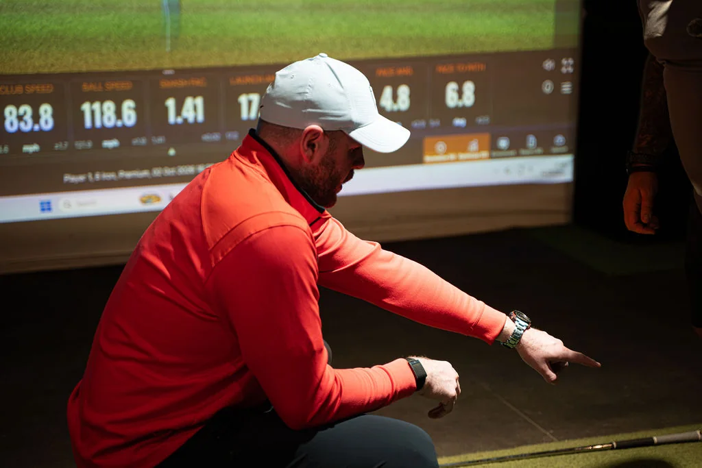 Coach crouching and pointing at TrackMan data on the screen during a golf coaching session at Evolution Golf Academy near Derby