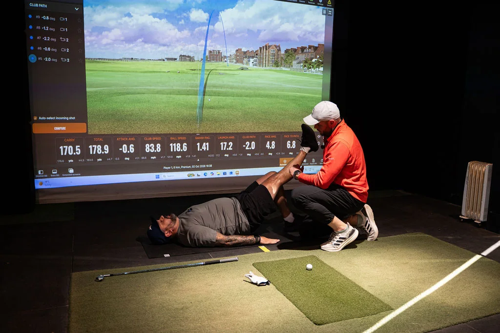 Coach stretching a golfer's leg on the mat as part of a golf fitness assessment at Evolution Golf Academy near Derby