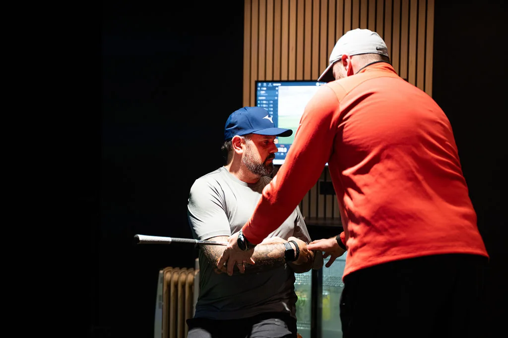 Coach guiding a seated golfer through a trunk rotation assessment with a club across the chest at Evolution Golf Academy near Derby
