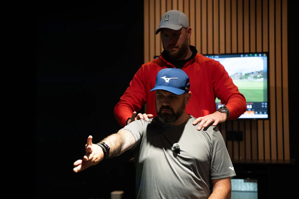 Coach guiding a golfer's shoulders from behind during a shoulder mobility check at Evolution Golf Academy near Derby