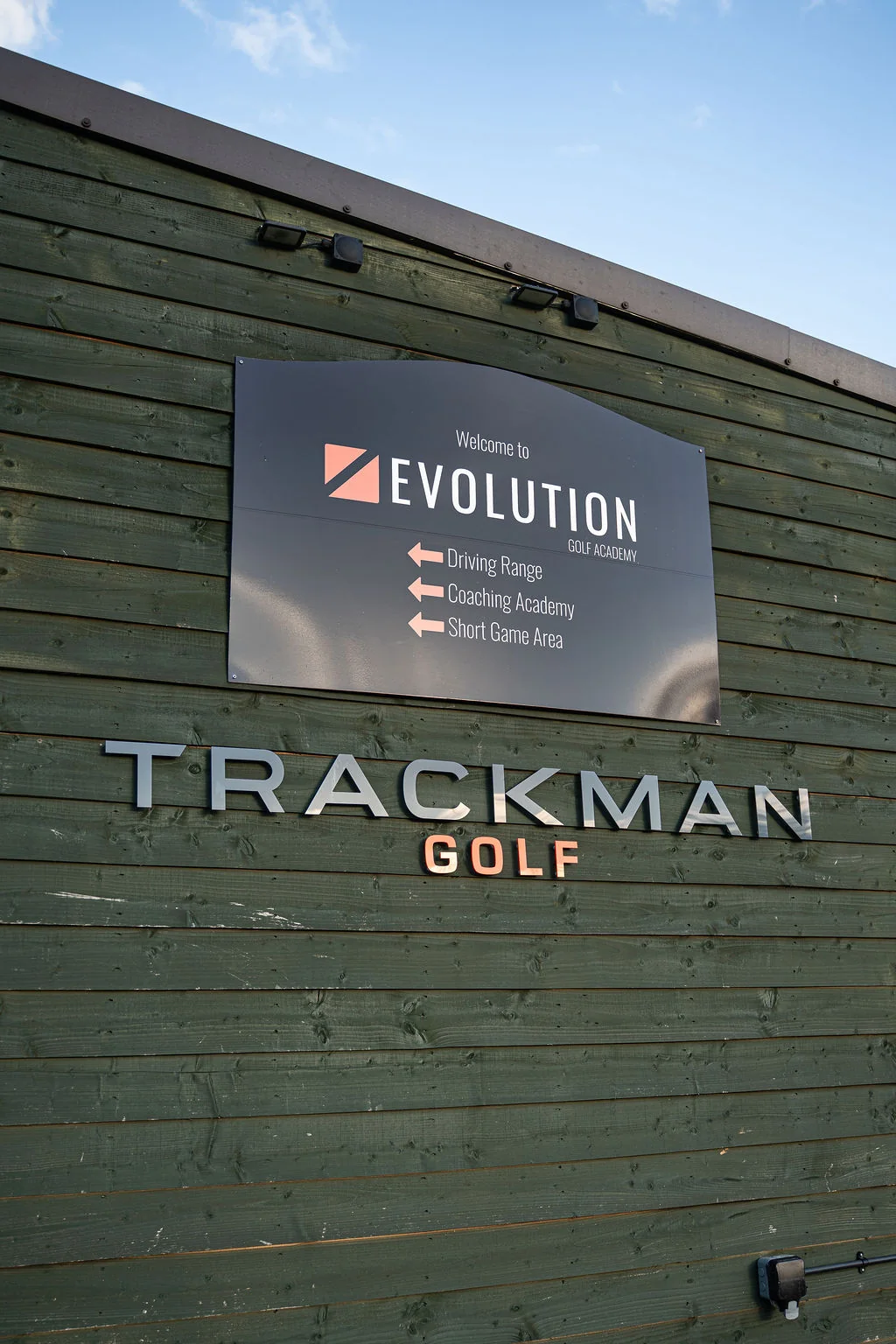 Evolution Golf Academy sign on the TrackMan Golf building showing driving range and coaching academy directions