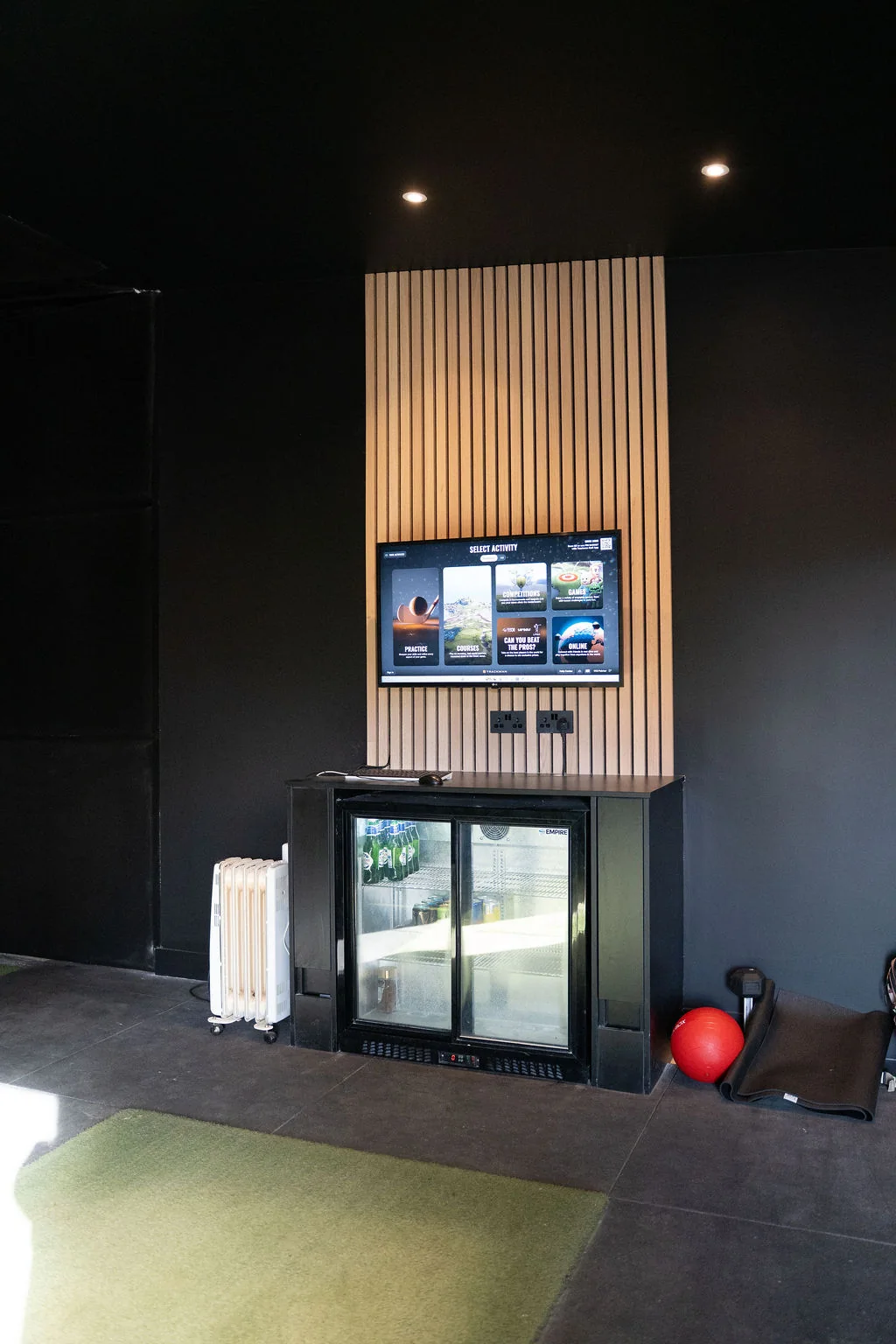 Indoor golf simulator bay with a hitting mat and TrackMan screen on a slatted wall at Evolution Golf Academy near Derby