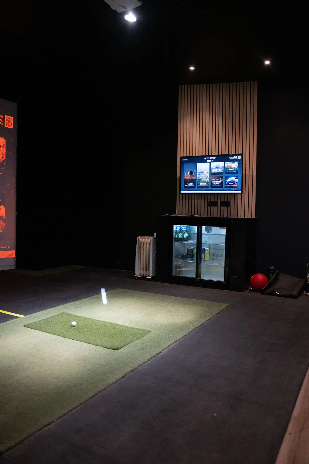 Indoor TrackMan simulator bay with a hitting mat, ball and drinks fridge at Evolution Golf Academy near Derby