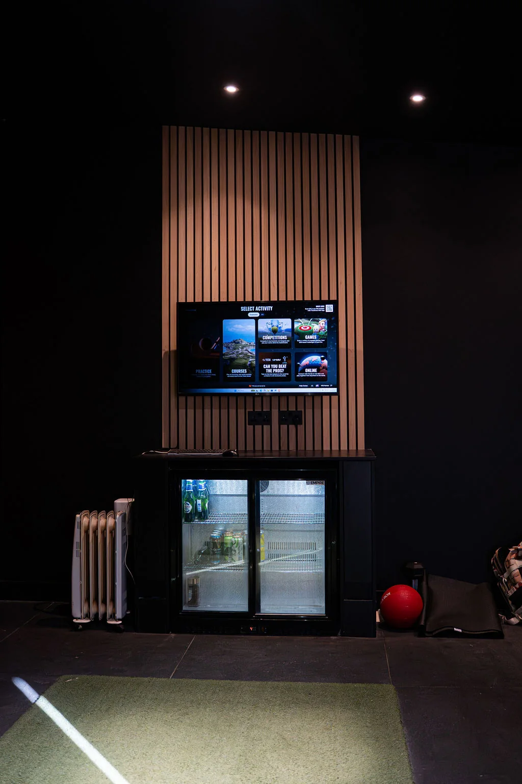 Simulator bay with the TrackMan screen on a slatted wall above a drinks fridge at Evolution Golf Academy near Derby