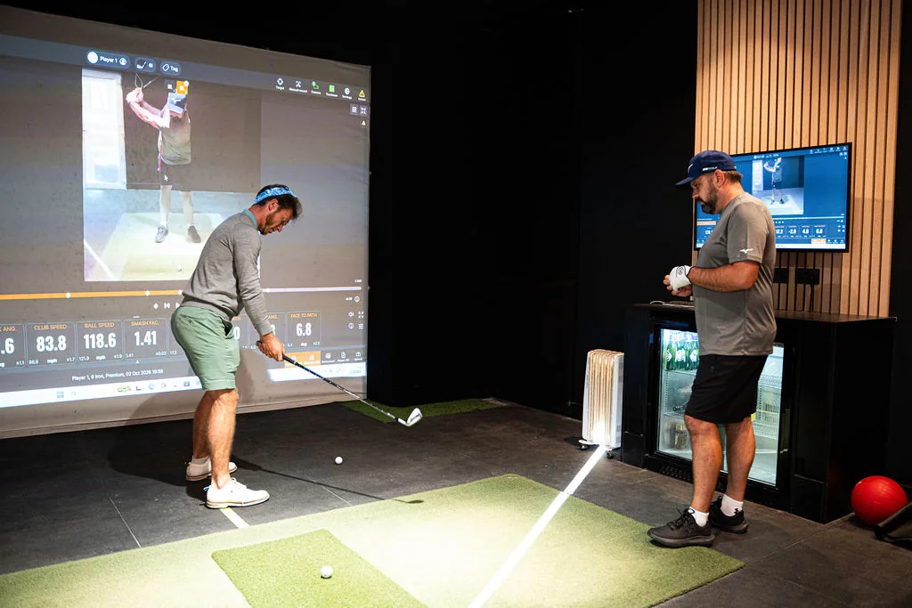 Golfer practising a shot while the coach watches in the simulator bay at Evolution Golf Academy near Derby