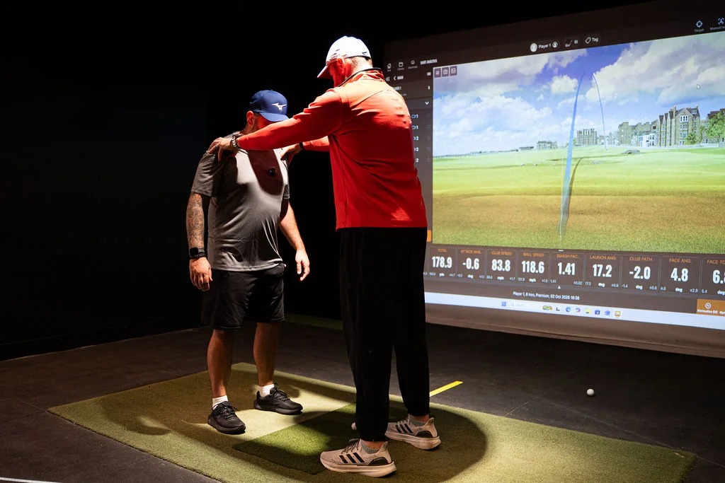 Coach adjusting a golfer's stance and posture on the hitting mat at Evolution Golf Academy near Derby