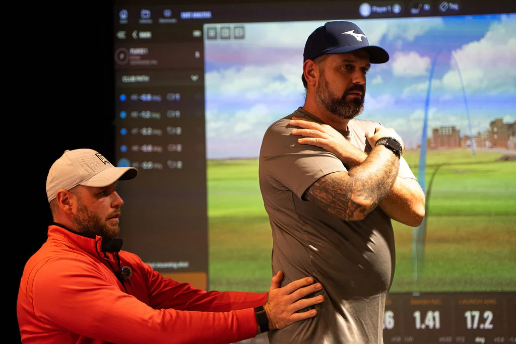 Coach guiding a golfer through a crossed arm rotation drill in front of the TrackMan screen at Evolution Golf Academy near Derby