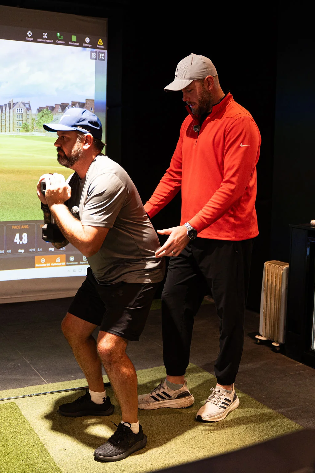 Strength coach supporting a golfer through a kettlebell squat in the TrackMan bay at Evolution Golf Academy near Derby