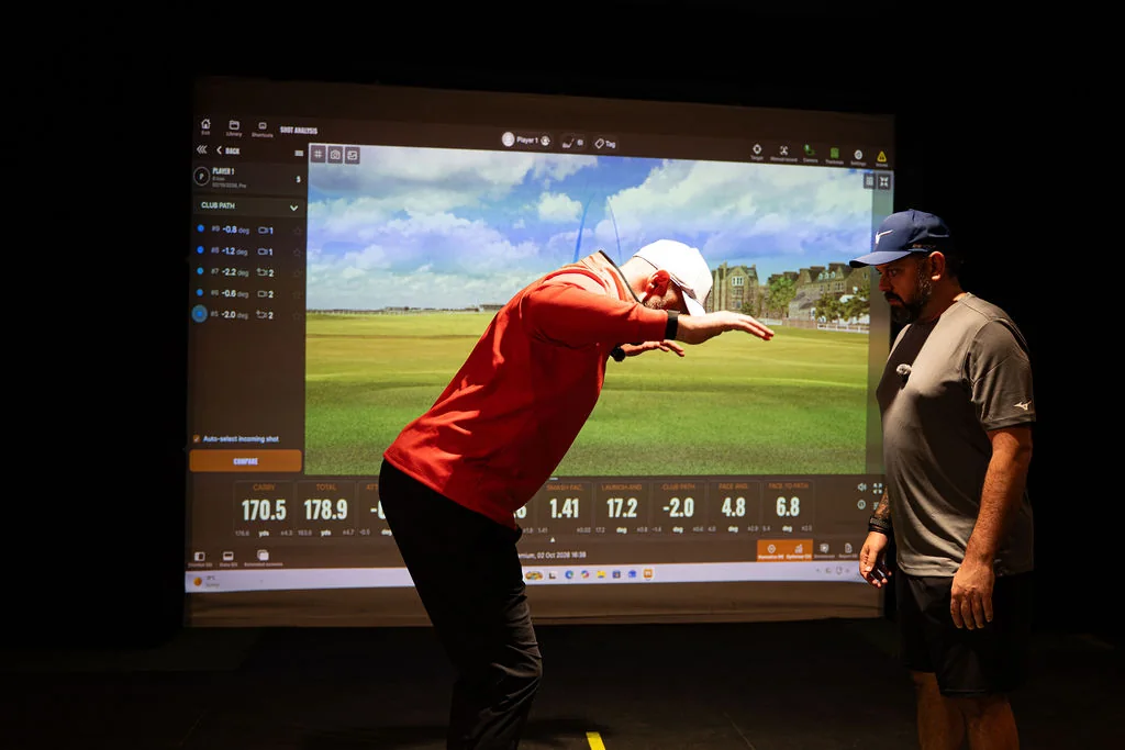 Coach demonstrating a hip hinge in front of the TrackMan screen while the golfer watches at Evolution Golf Academy near Derby