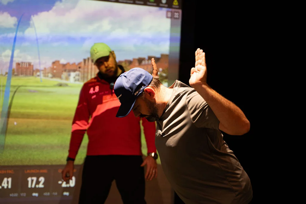 Coach and golfer demonstrating an arm position drill in front of the simulator screen at Evolution Golf Academy near Derby