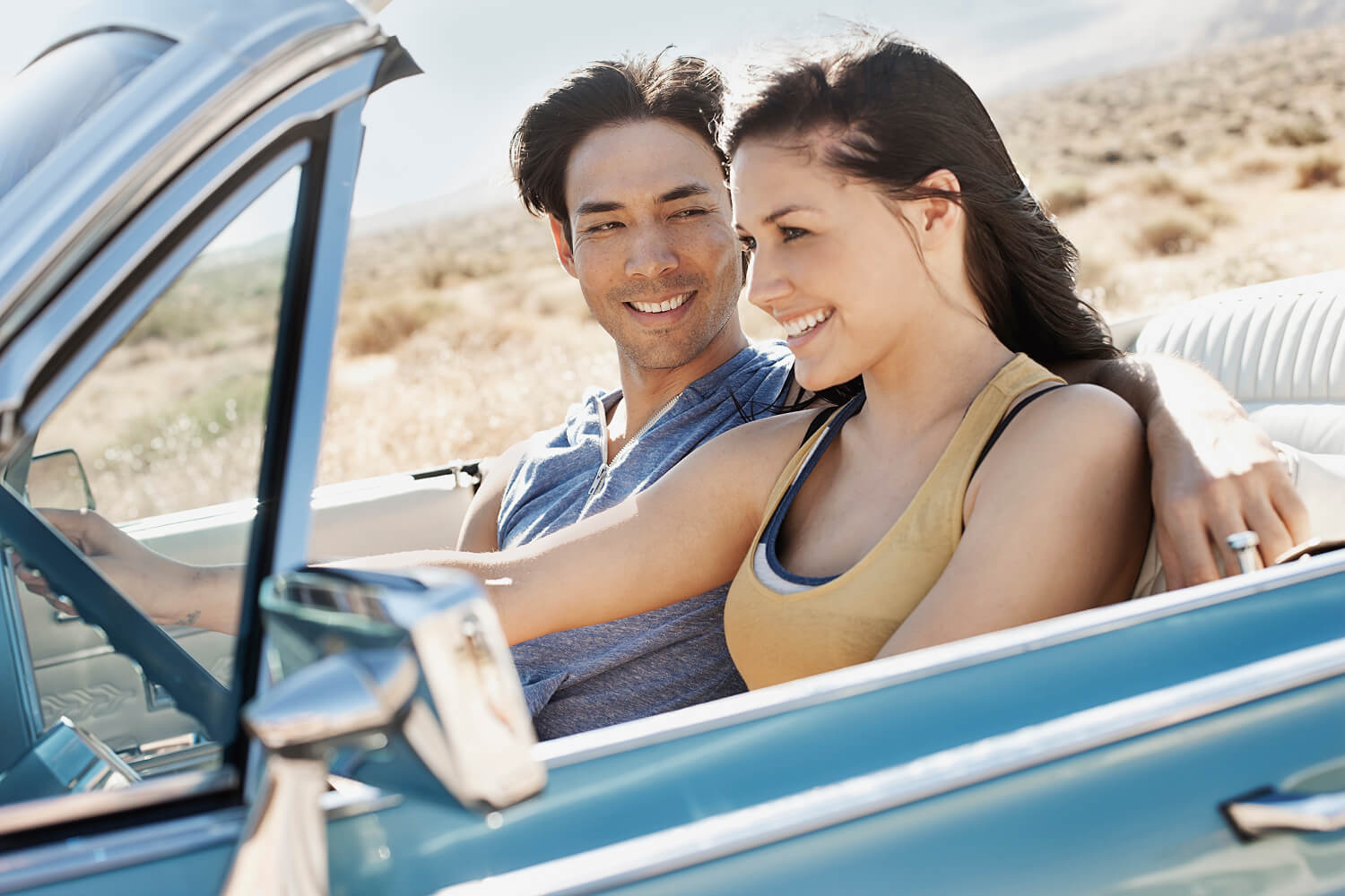 Young couple standing together beside a classic car.