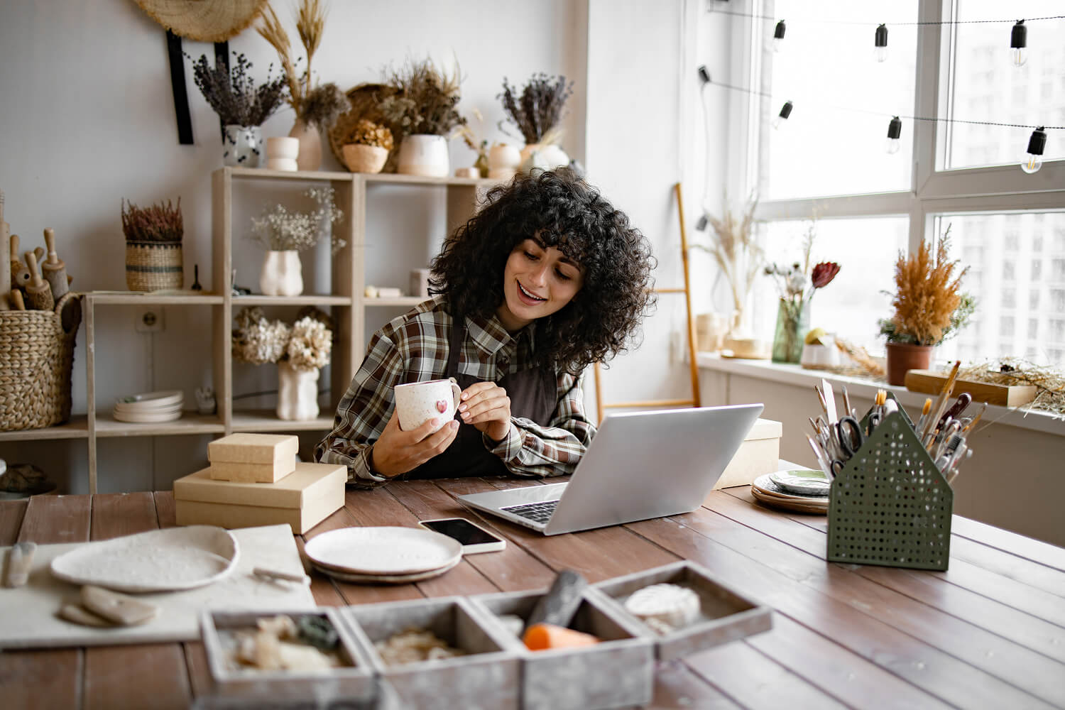 Young ceramic shop owner using a laptop while working in their store.
