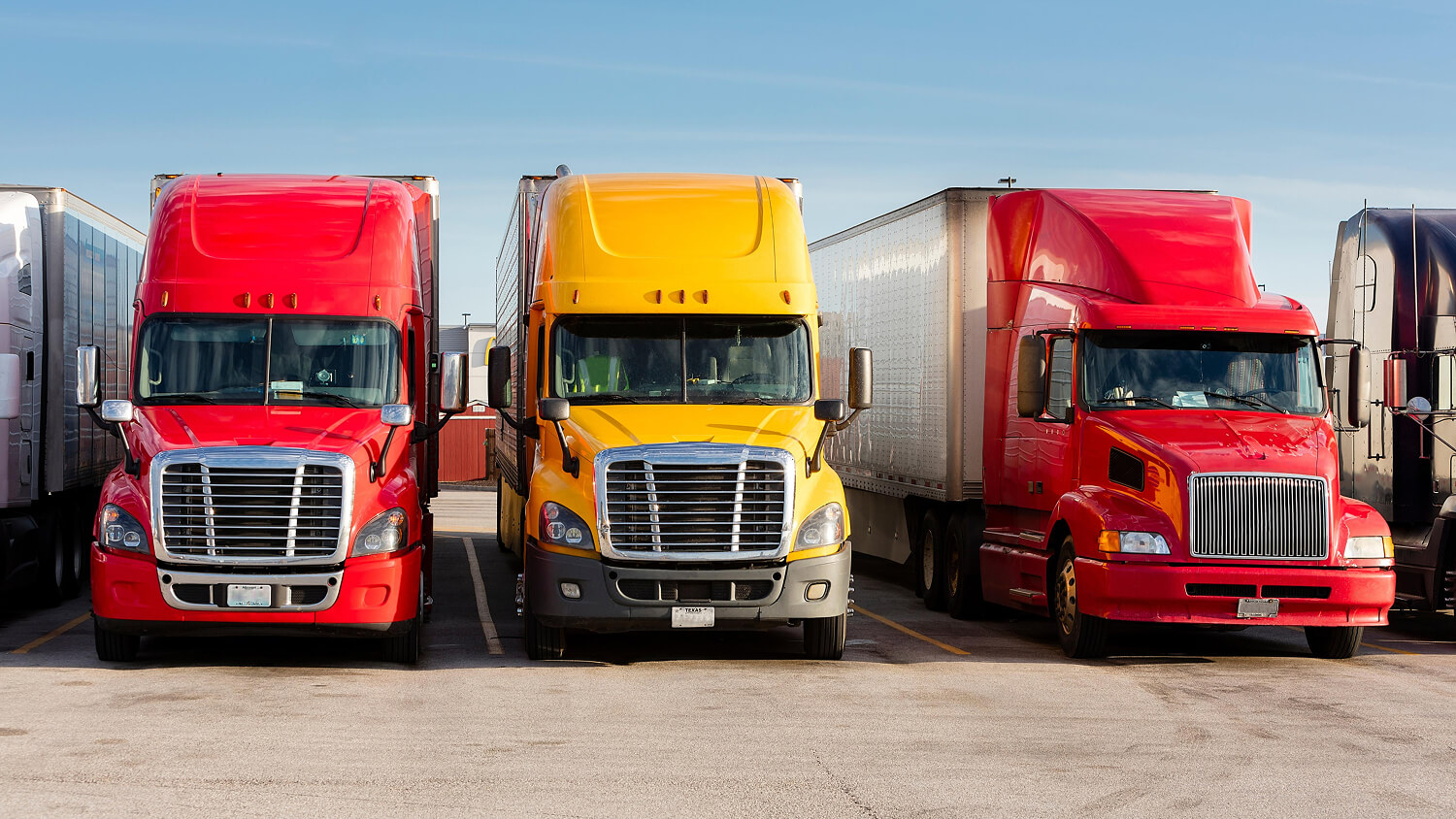 Three semi-trucks parked in a commercial lot.