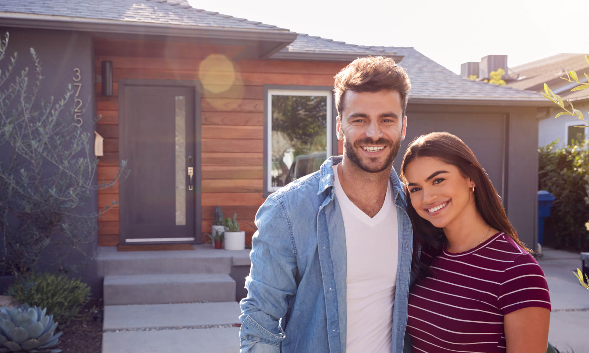 Young couple smiling in front of their home.