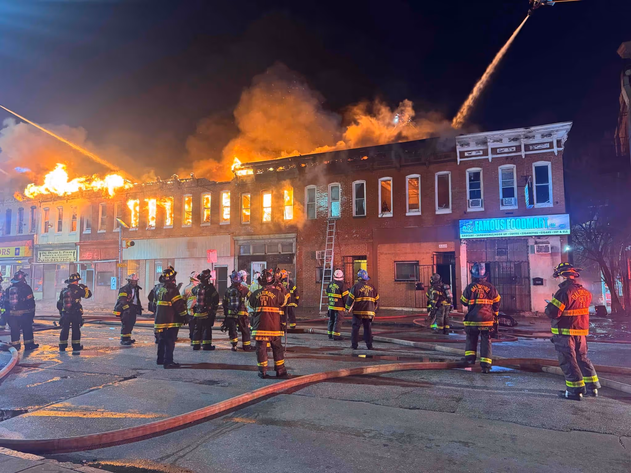 Firefighters from Baltimore City FD at night battling a large blaze engulfing a two-story row building.