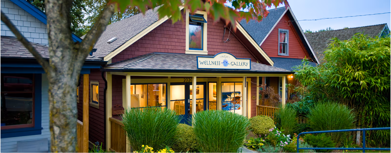 Exterior of Inlet Wellness Gallery building with plants and trees in the foreground at dusk.