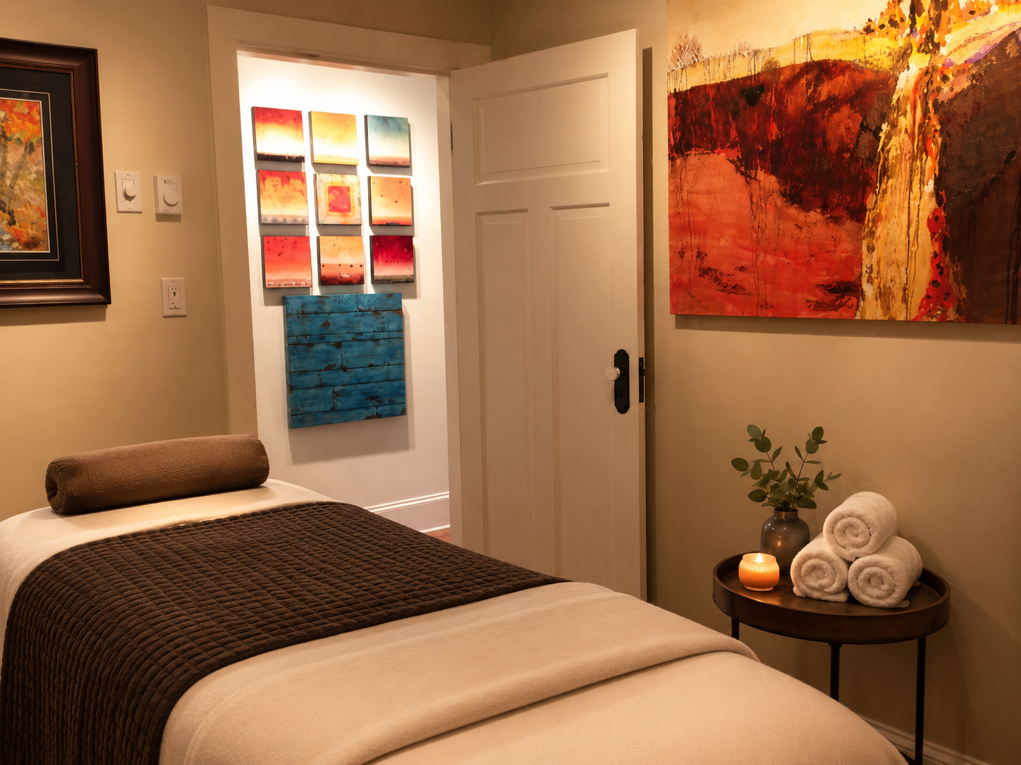 Serene wellness treatment room with a neatly made massage table, folded towels on a small side table, soft neutral decor and gentle lighting creating a calming, spa-like atmosphere.