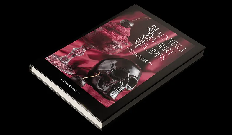 Book titled 'Haunting Dessert Recipes' with a skull and dessert on the cover over red fabric.