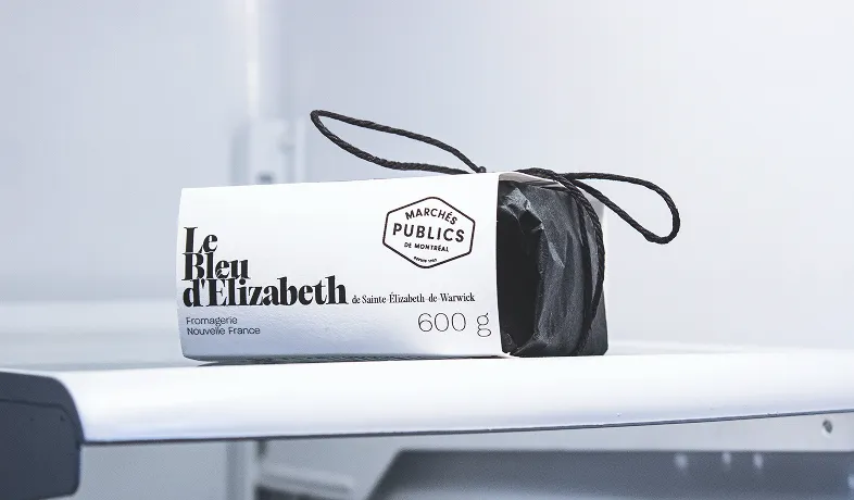 Le Bleu d’Elizabeth cheese wrapped in white label with black string on a white surface.