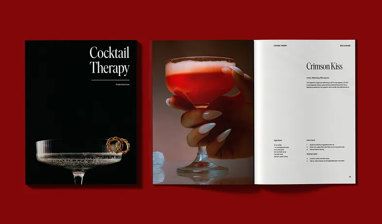 Open cocktail recipe book showing a hand holding a red drink and a page titled Crimson Kiss.