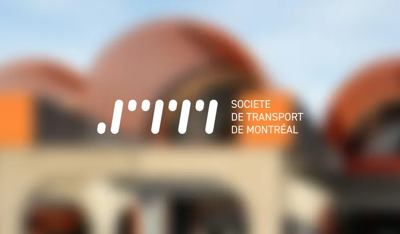 Logo of Société de Transport de Montréal in white over blurred background of orange curved roofs.