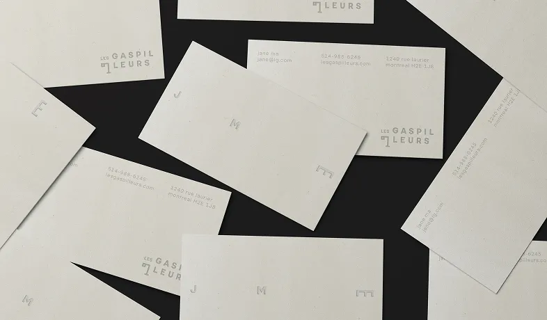 Scattered minimalistic business cards with light background and subtle text on a dark surface.