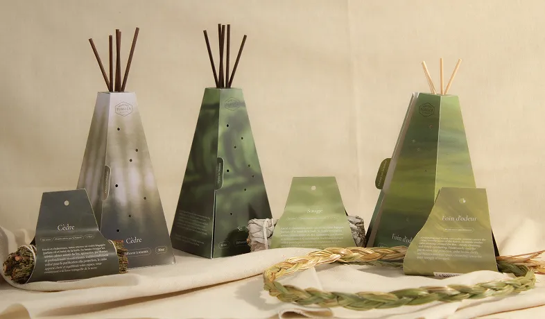 Three green and brown reed diffuser sets with greenery and braided grass on beige fabric.