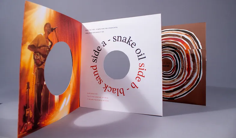 Open vinyl record cover showing a musician, text spiral, and colorful circular disc artwork.
