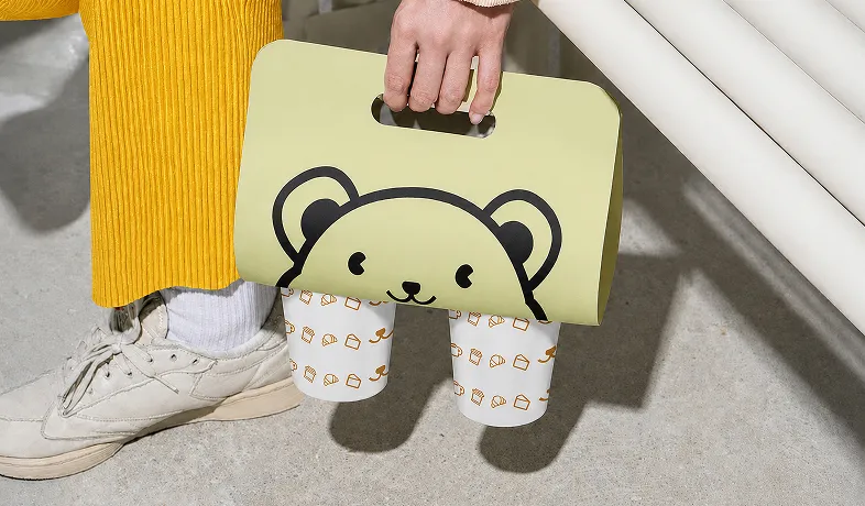 Person in yellow pants holding green bear-themed bag with two decorated drink holders.